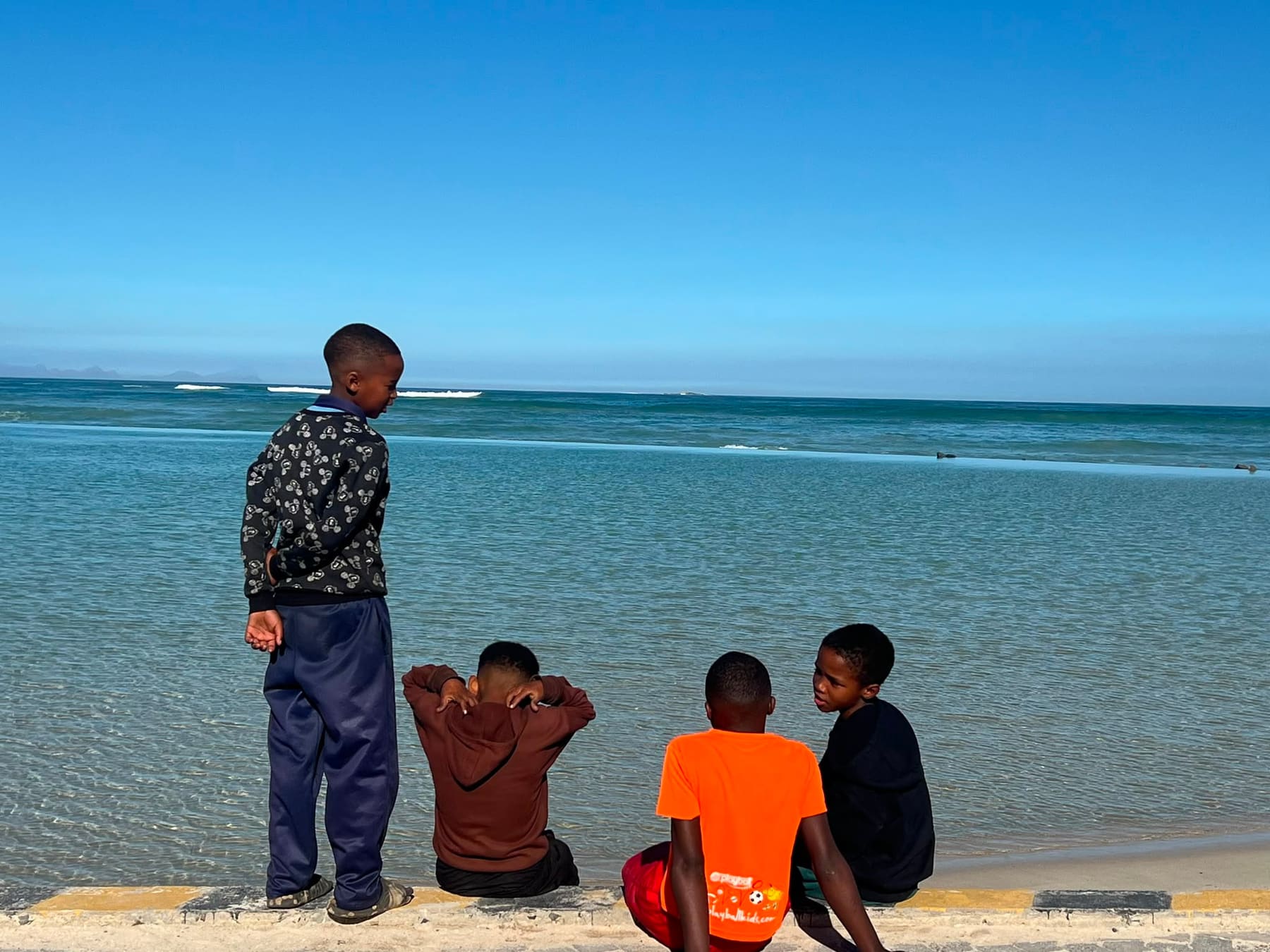 Children sitting on the sea wall looking out at the bay
